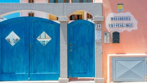 Un edificio con due ampie porte blu, un cartello con la scritta "RESIDENZA CRISTAL BLU" e una piccola cassetta postale.