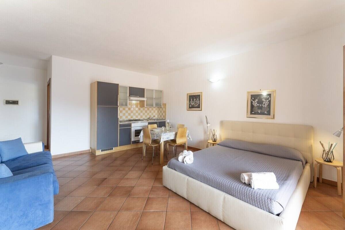 A hotel room with a bed, a sofa, a dining table with chairs, and a kitchenette.