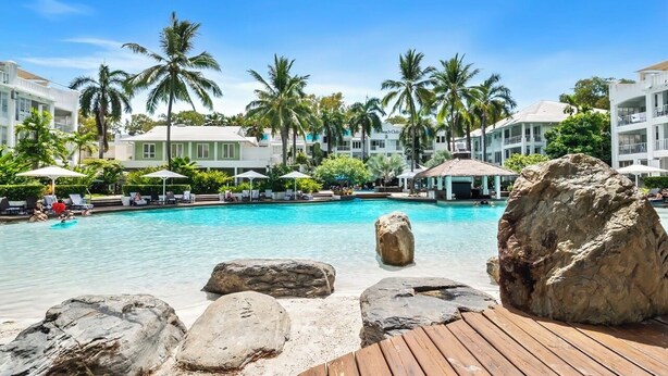 Une piscine d’hôtel agrémentée de gros rochers, de palmiers et d’une terrasse en bois.