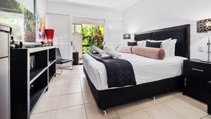 Une chambre moderne avec un grand lit, un ventilateur de plafond, une bibliothèque et une vue sur la verdure grâce aux portes coulissantes.