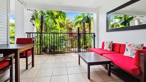 Un balcon agrémenté d’un canapé rouge et d’une table à manger, le tout entouré d’une végétation tropicale luxuriante.