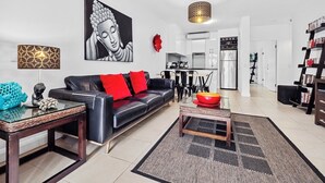 Un salon moderne avec un canapé en cuir noir, des coussins rouges, une table basse en verre et un tableau représentant un Bouddha accroché au mur.