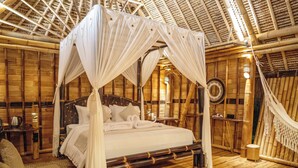 A large bed with a canopy, wooden walls, and a thatched roof.
