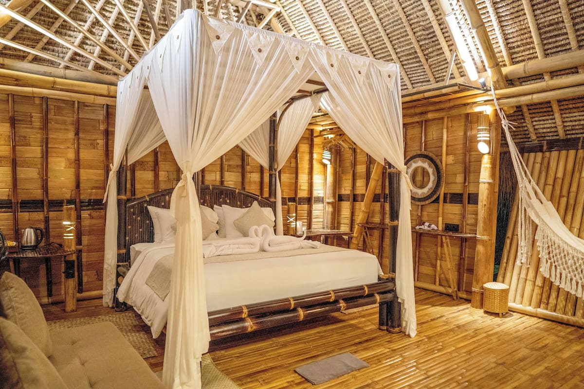 A large bed with a canopy, wooden walls, and a thatched roof.