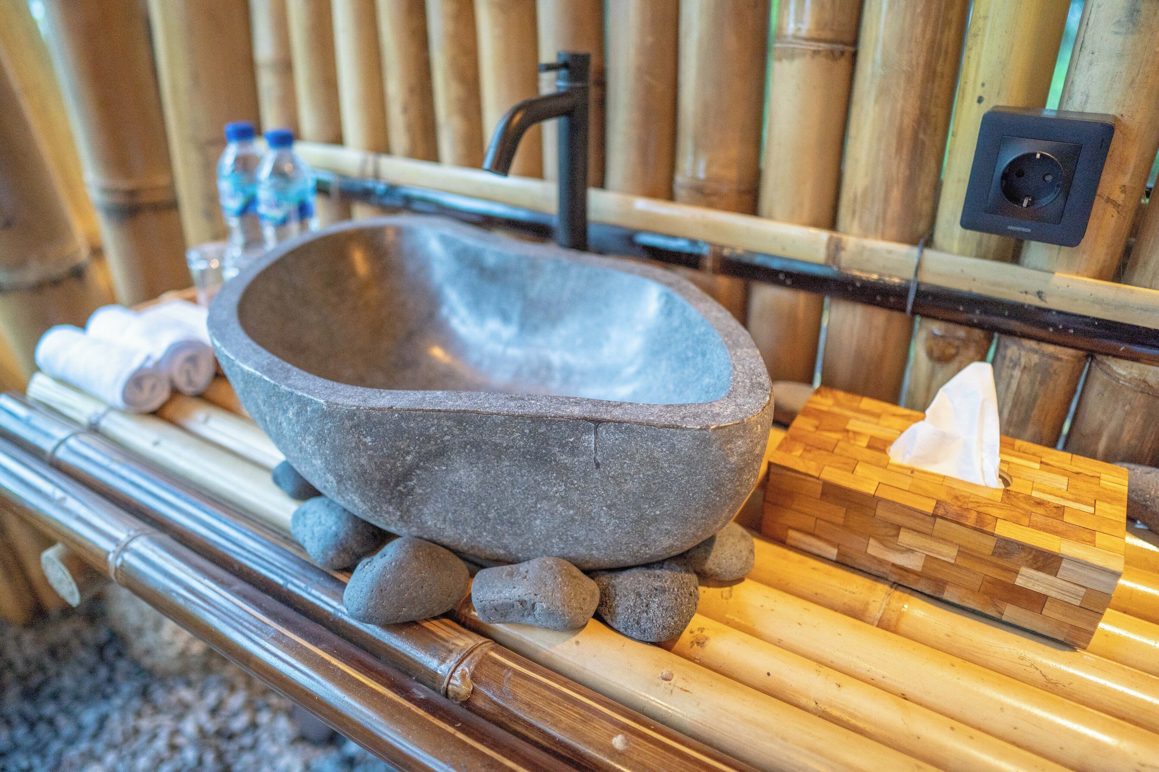 A stone basin with a wooden stool, bamboo flooring, a bamboo wall, and a tissue box.