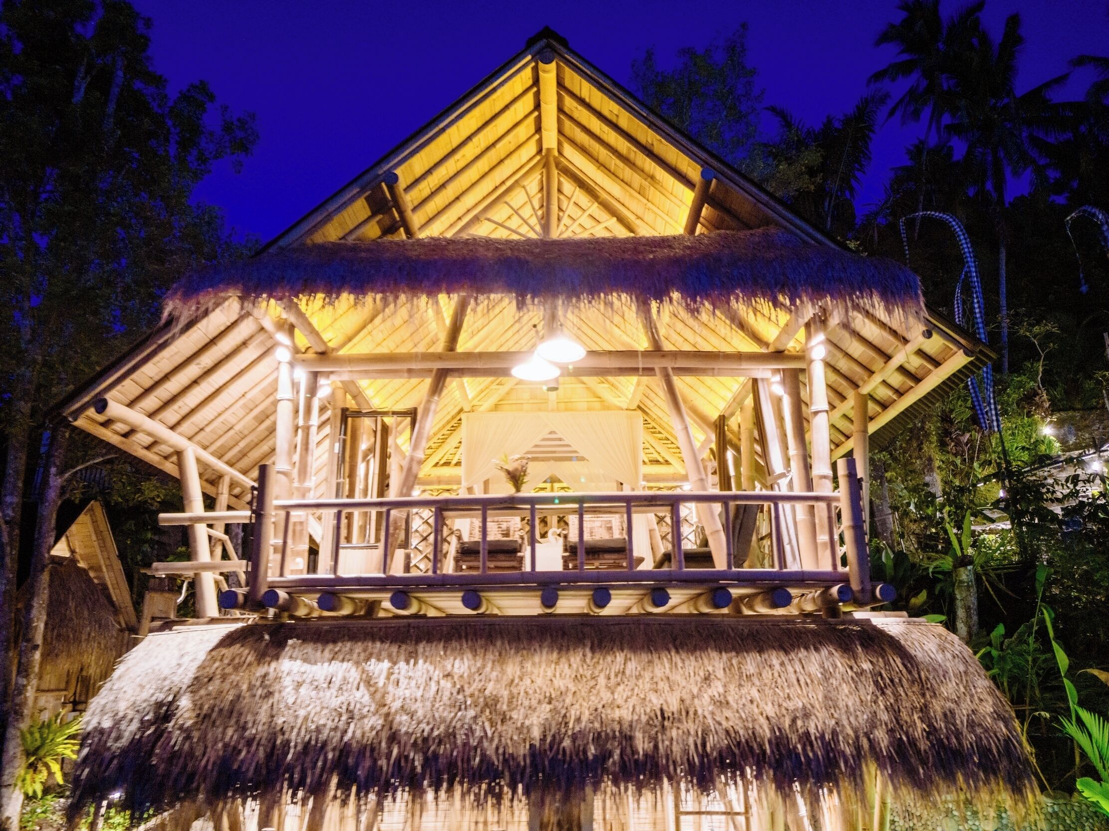 A thatched-roof structure with a balcony, surrounded by tropical vegetation.