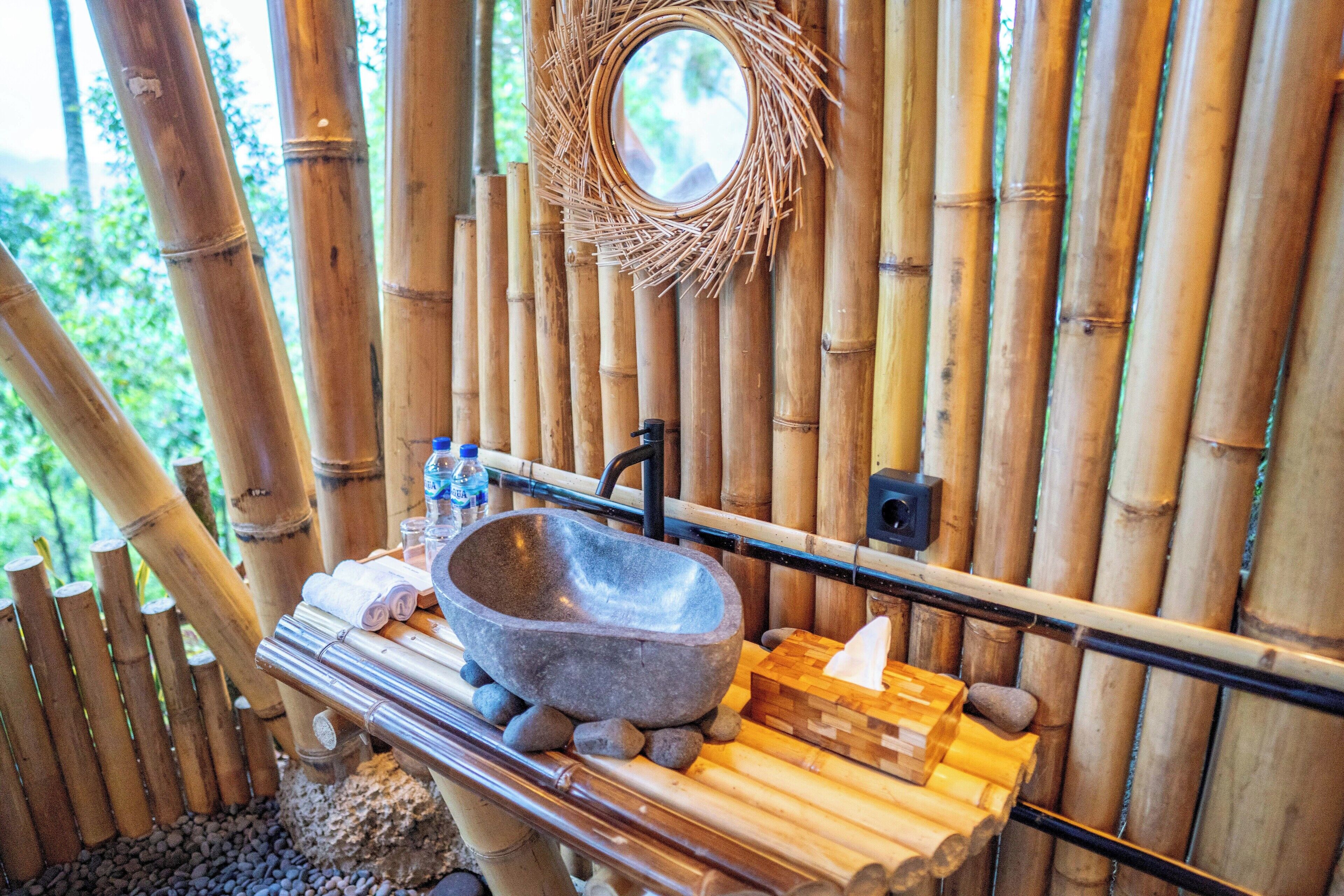 A bathroom with a stone sink, bamboo walls, a mirror, and a wooden shelf with toiletries.