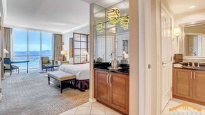 A hotel room with a large window, a bed, a desk, and a bathroom with a mirror and sink.