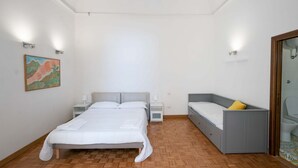 Une chambre avec un grand lit, une table de chevet, une commode, un petit bureau, une chaise et une salle de bain avec des toilettes et un lavabo.