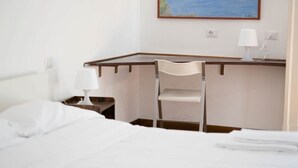 A hotel room with a bed, a desk, a chair, and a nightstand with a lamp.