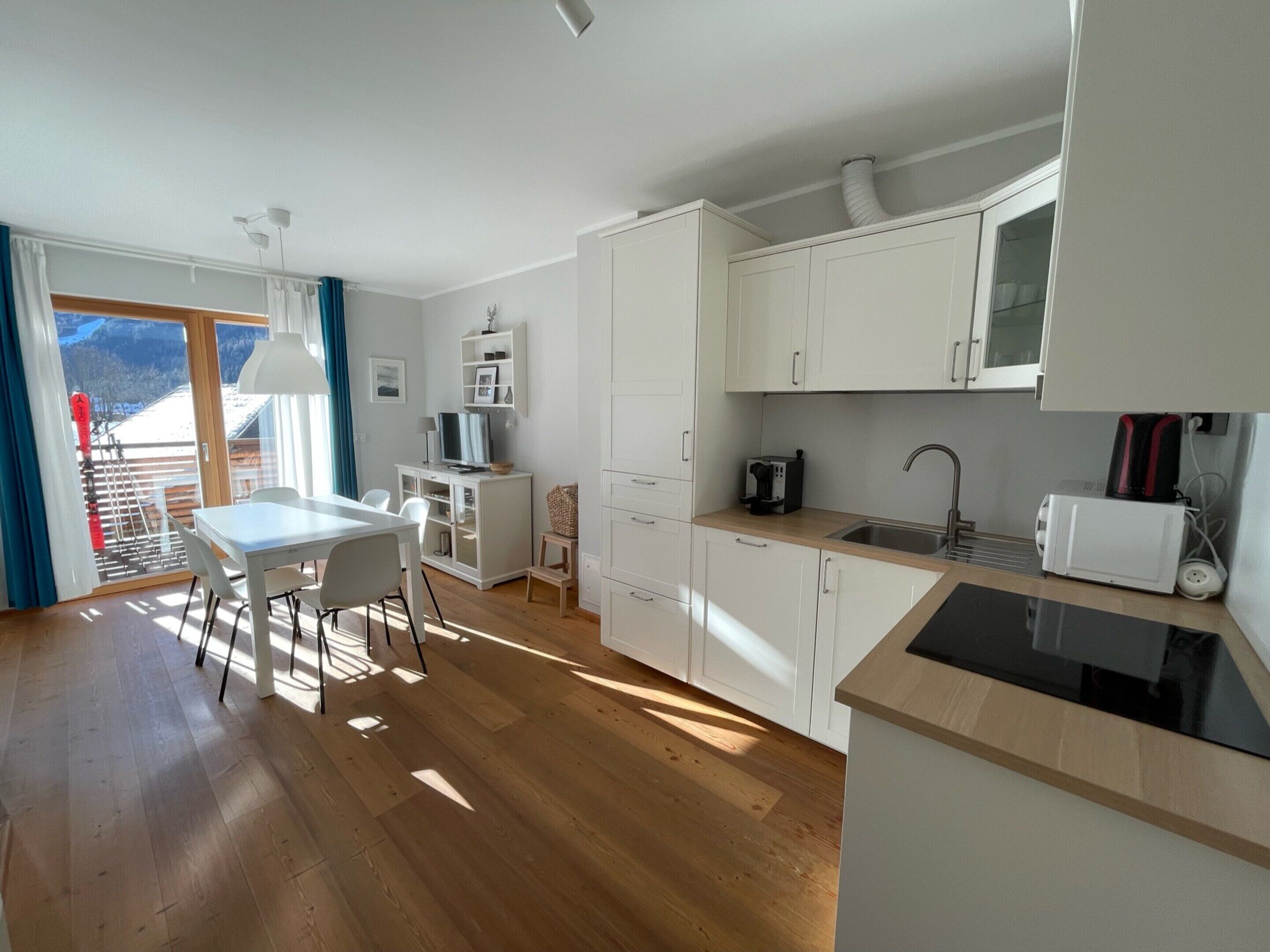 Una cocina moderna con armarios blancos, un comedor con mesa y sillas, y vistas al exterior a través de una puerta corrediza de vidrio.