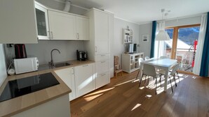 A modern kitchen with white cabinets, a built-in microwave, and a coffee maker. There's a dining area with a table and chairs, and a balcony with a view of the mountains. - Exclusive Apartment With Scenic View (Bad Kleinkirchheim)
