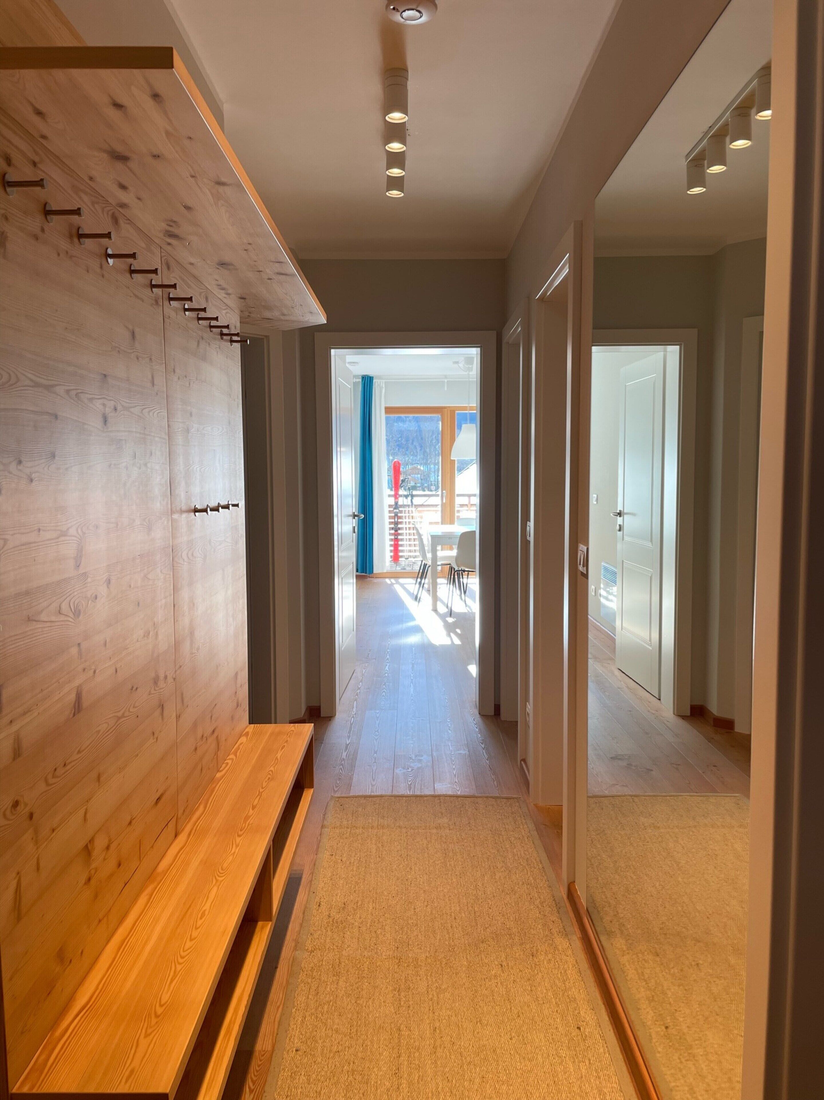 A modern hallway with wooden paneling, a bench, and a carpeted floor leading to a bright room with a view of the outdoors.