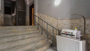Un escalier avec une rampe en métal, un chauffe-eau sur la droite et un mur en pierre.