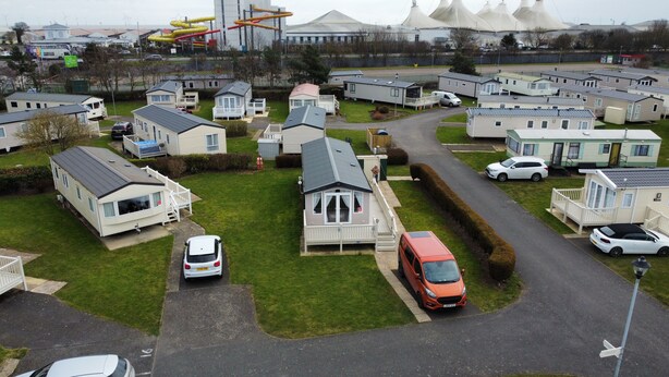 A residential area with mobile homes, a road, and a white car parked in front of a house. - Butlins-skegness-luxury 8 Berth Caravan-dog Friend (Skegness)