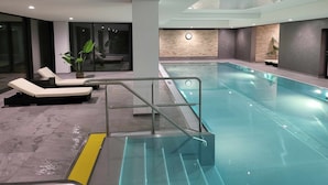 A modern indoor swimming pool with a glass barrier, lounge chairs, and a clock on the wall. - FeWo Eulenhorst - Holiday enjoyment in the vacation resort at Schluchsee (with pool) (Schluchsee)