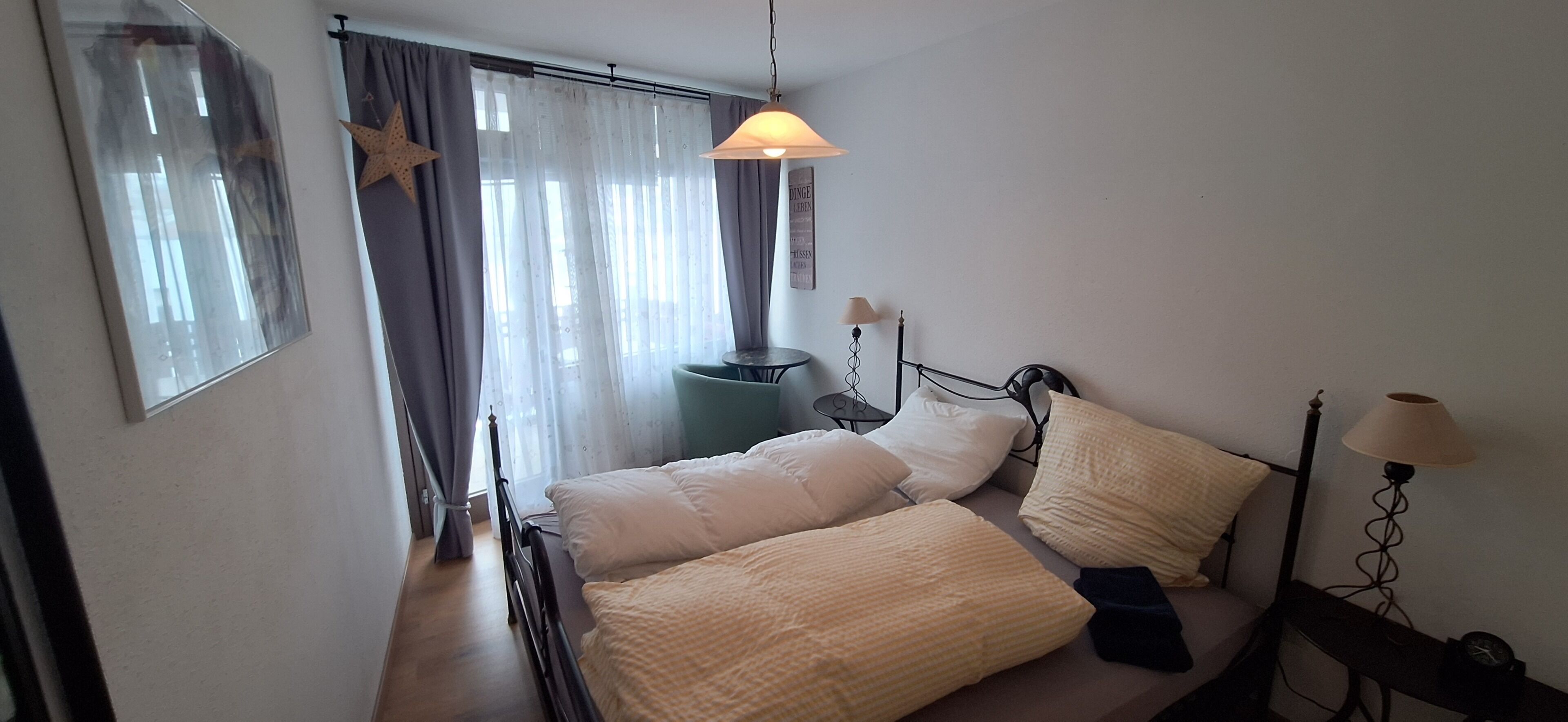 Ein Schlafzimmer mit Bett, Nachttischlampen, einem Fenster mit Vorhängen und einer Stern-Dekoration an der Wand.