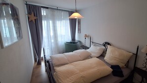 A bedroom with a bed, bedside lamps, a window with curtains, and a wall-mounted star decoration. - FeWo Eulenhorst - Holiday enjoyment in the vacation resort at Schluchsee (with pool) (Schluchsee)