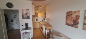 A compact kitchen with wooden cabinets, a coffee machine, and wall-mounted artwork.