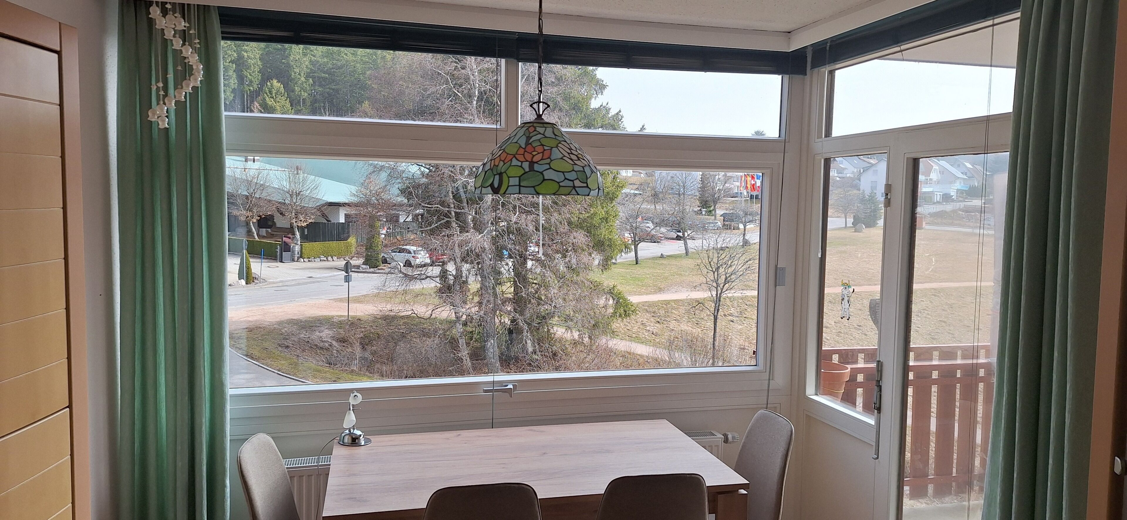 Ein Zimmer mit großem Fenster, einem Tisch, Stühlen und einer Pendelleuchte.