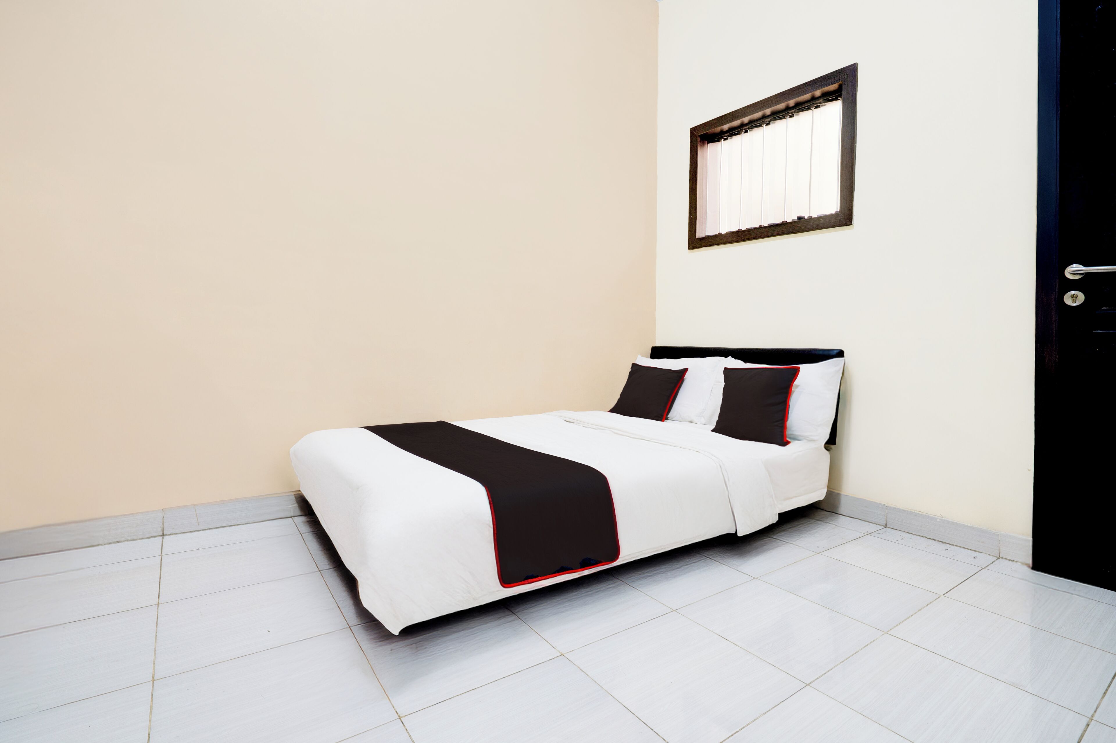A neatly made bed with a black and white bedspread and pillows, a window with blinds, and a door with a handle.