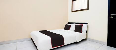 A neatly made bed with a black and white bedspread and pillows, a window with blinds, and a door with a handle.
