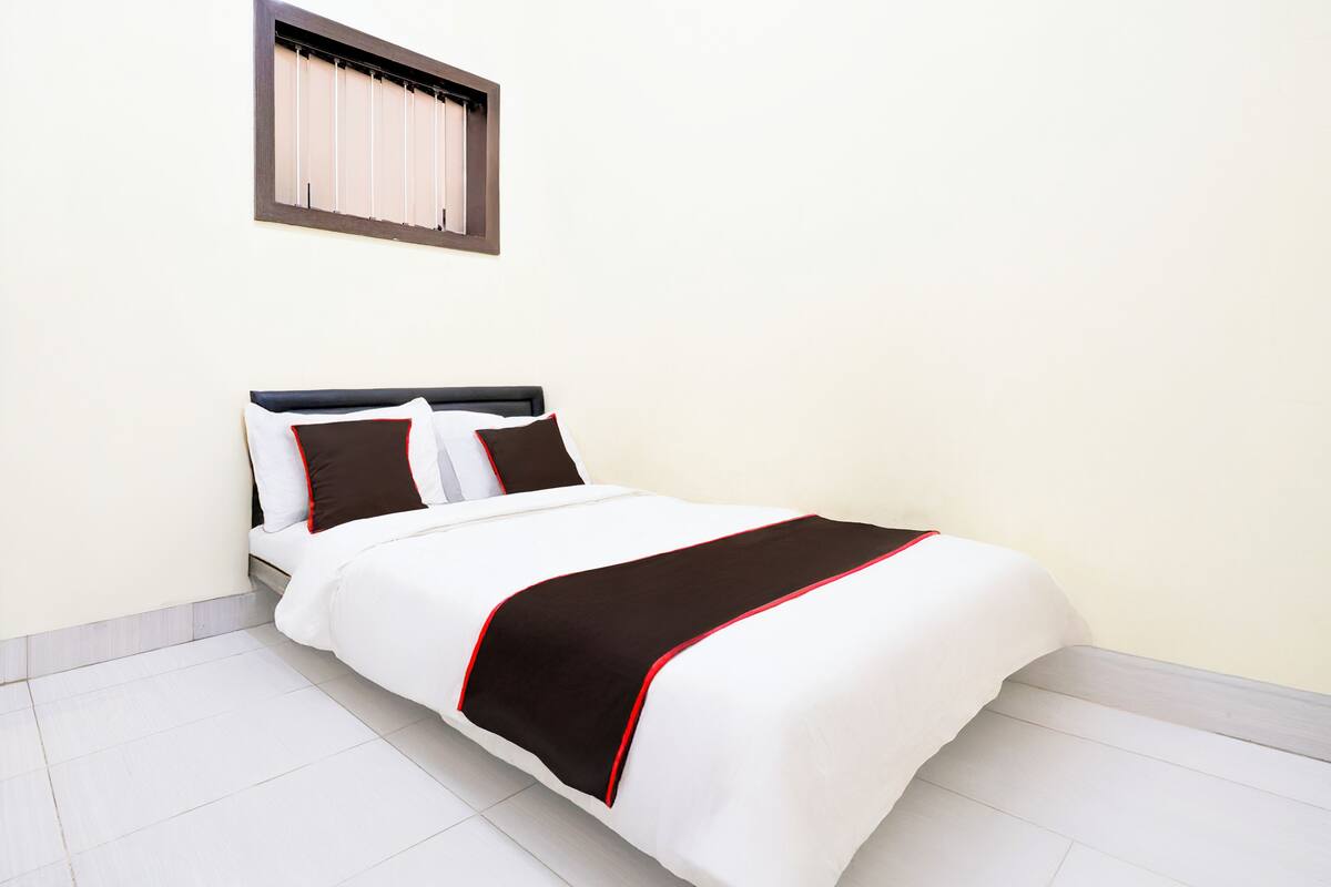 Cama bem arrumada com colcha branca e marrom, cabeceira e duas almofadas.