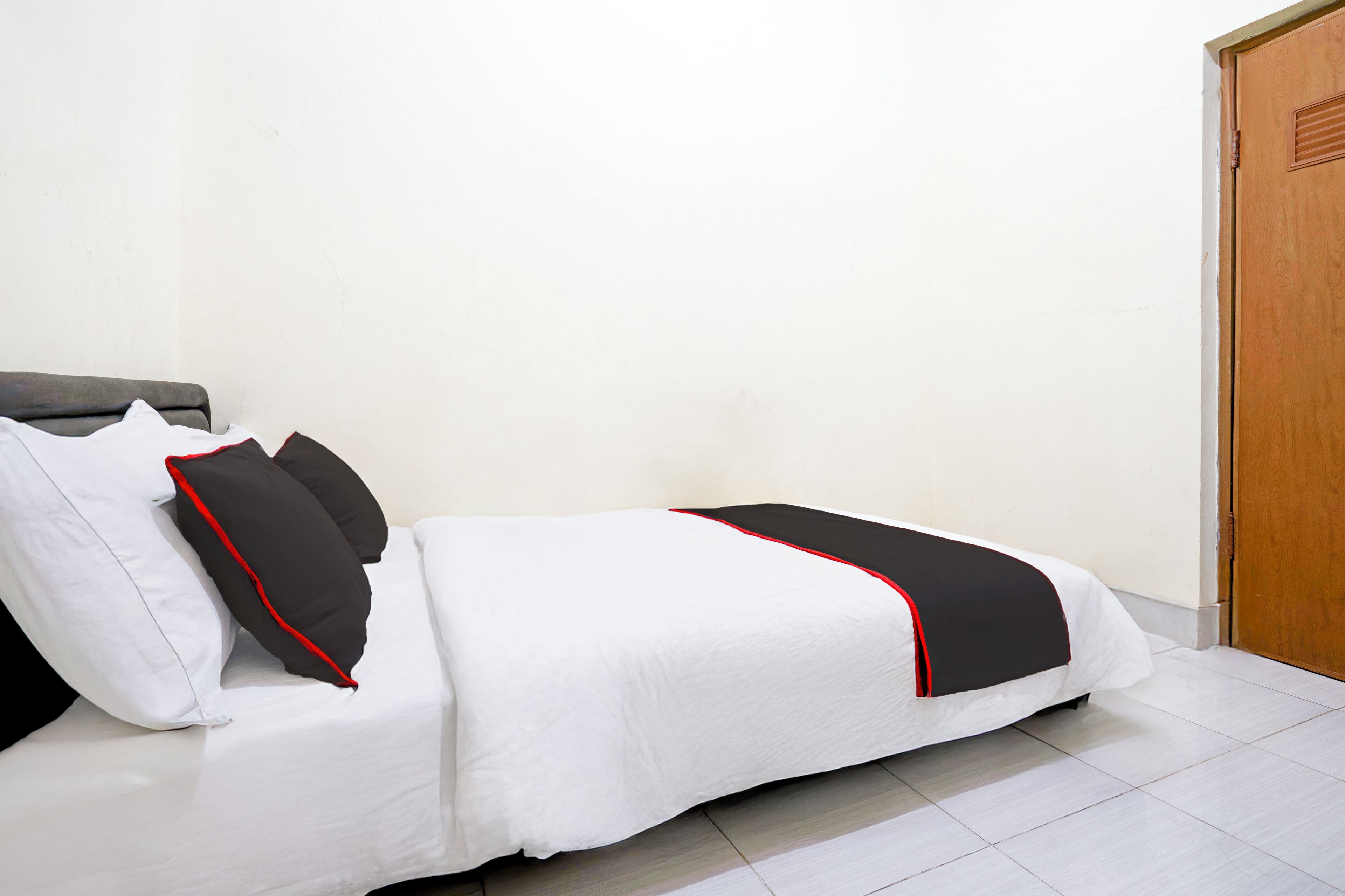 A neatly made bed with white bedding and black accents, a wooden door, and a tiled floor.