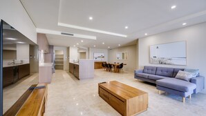 A modern living room with a sofa, coffee table, and a dining area with chairs and a table. - Casa Di Marco Polo - 3 Bedroom Apartment (Mandurah)
