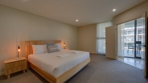 A modern hotel room with a large bed, bedside tables, a view of the outdoor balcony, and a sliding glass door. - Casa Di Marco Polo - 3 Bedroom Apartment (Mandurah)