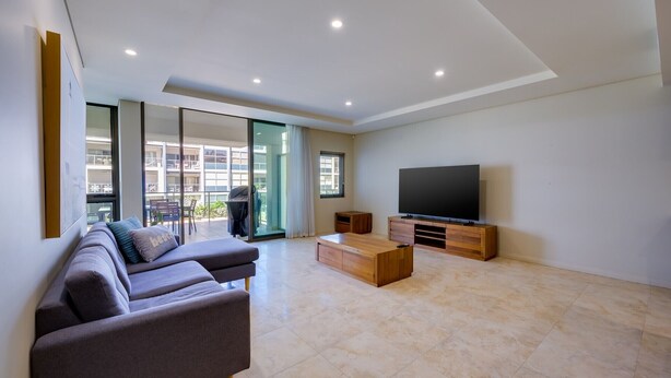A spacious living room with a large flat-screen TV, a sofa, and a coffee table. - Casa Di Marco Polo - 3 Bedroom Apartment (Mandurah)