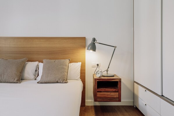 Un lit bien fait, avec une tête de lit en bois, une table de chevet avec une lampe et une petite étagère.