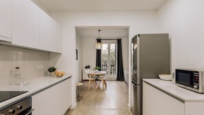 A modern kitchen with white cabinets, a built-in oven, a microwave, and a dining area with a table and chairs.
