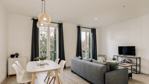 A modern living room with a dining table, grey sofa, and a TV on a stand.