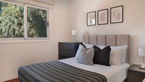 A bedroom with a bed, a nightstand, a dresser, and a window with a view of trees.