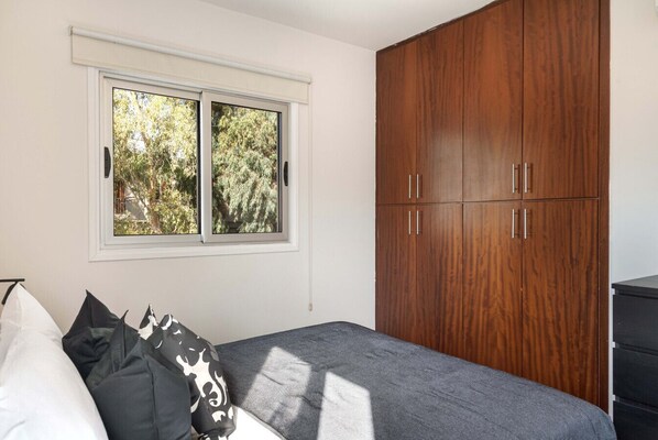 A bedroom with a bed, a window with a view of trees, and a wooden wardrobe.
