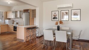 A modern kitchen with a central island, bar stools, a dining table with chairs, and three framed artworks on the wall.