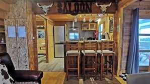 A rustic interior with a bar area labeled "SALON," wooden furniture, and a view of the outside.