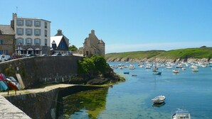 A coastal town with a historic stone tower, a fortified wall, and a harbor filled with boats.