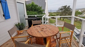 A wooden deck with a round table and chairs, a grill, and a view of the surrounding landscape.