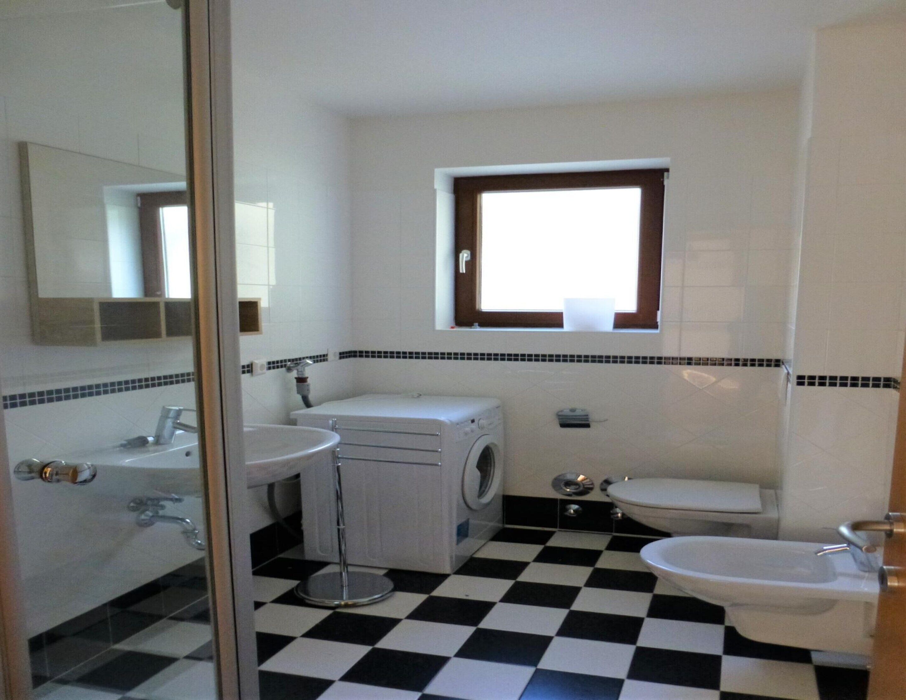 Un baño con piso a cuadros, una ventana, un lavabo, un inodoro y una lavadora.