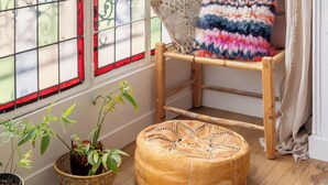 A corner room with a wooden chair, a colorful cushion, a potted plant, and a woven ottoman. - Behind the Stained Glass, by Veeve (Paris)