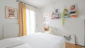 A bedroom with a bed, a radiator, a bookshelf, and a door leading to another room. - Behind the Stained Glass, by Veeve (Paris)
