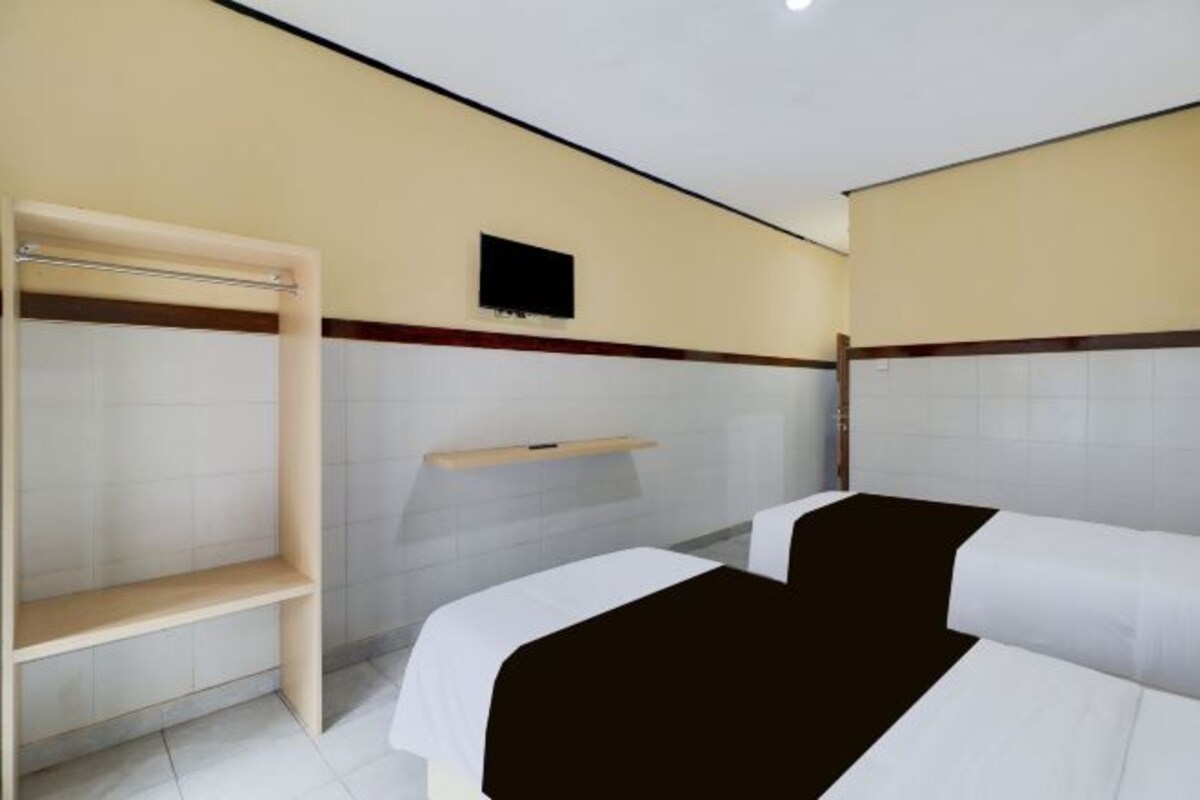 Une chambre d’hôtel avec deux lits, un téléviseur fixé au mur et une étagère au-dessus des lits.