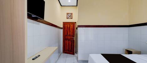 A narrow hallway leading to a bedroom with a bed, a wooden door, and a small bedside table.