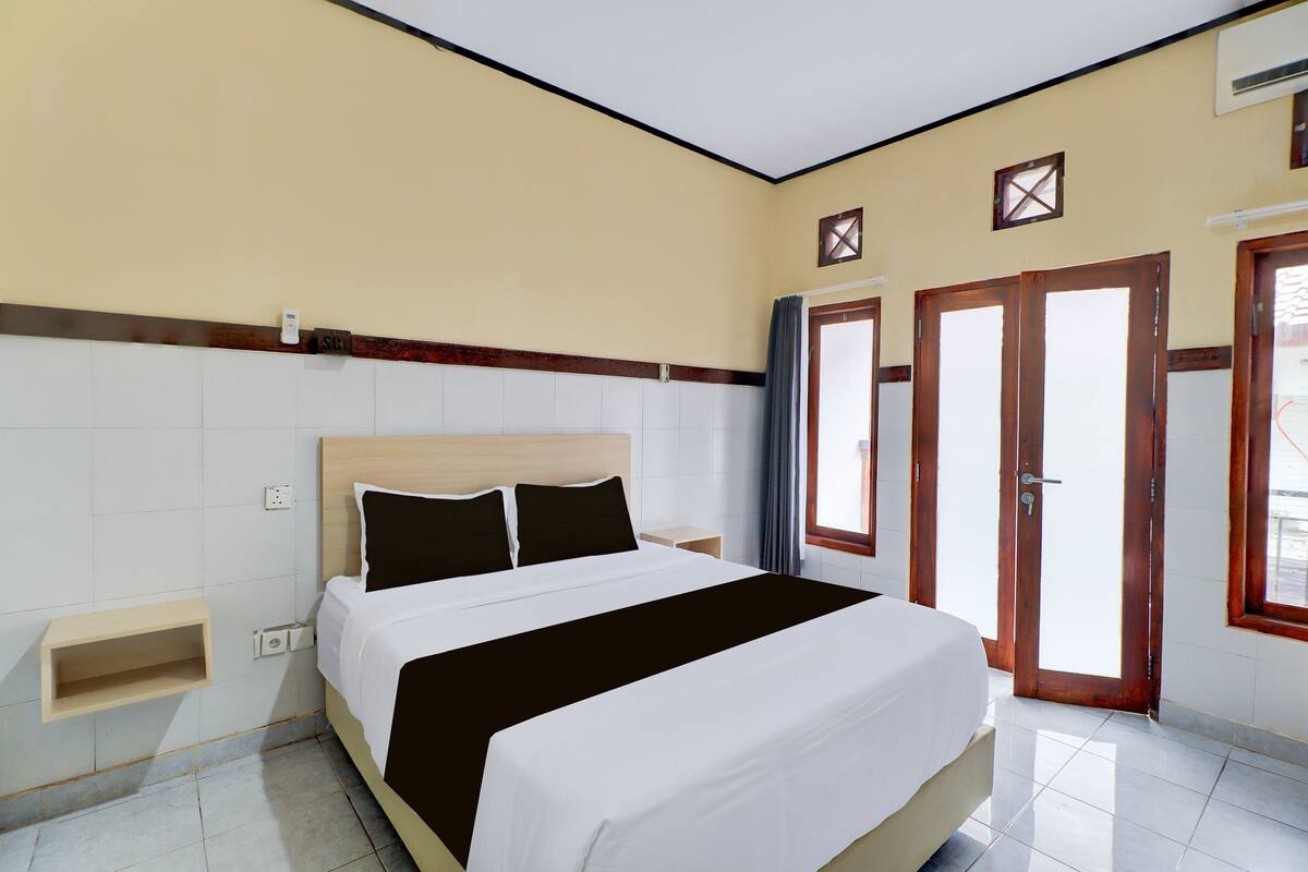 Habitación de hotel con cama, mesita de noche, estante en la pared y puerta con vistas.