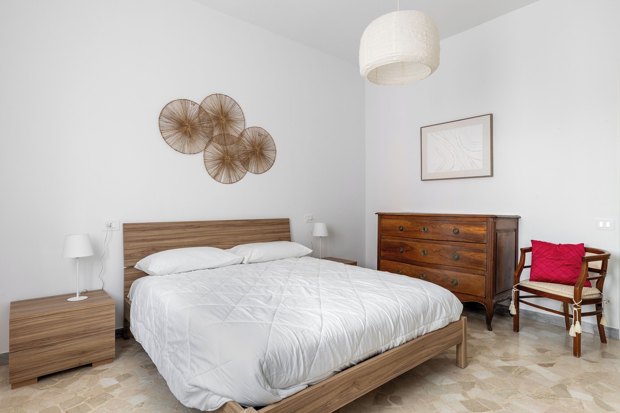 A bedroom with a wooden bed, a nightstand, a dresser, a chair, and a wall art piece.