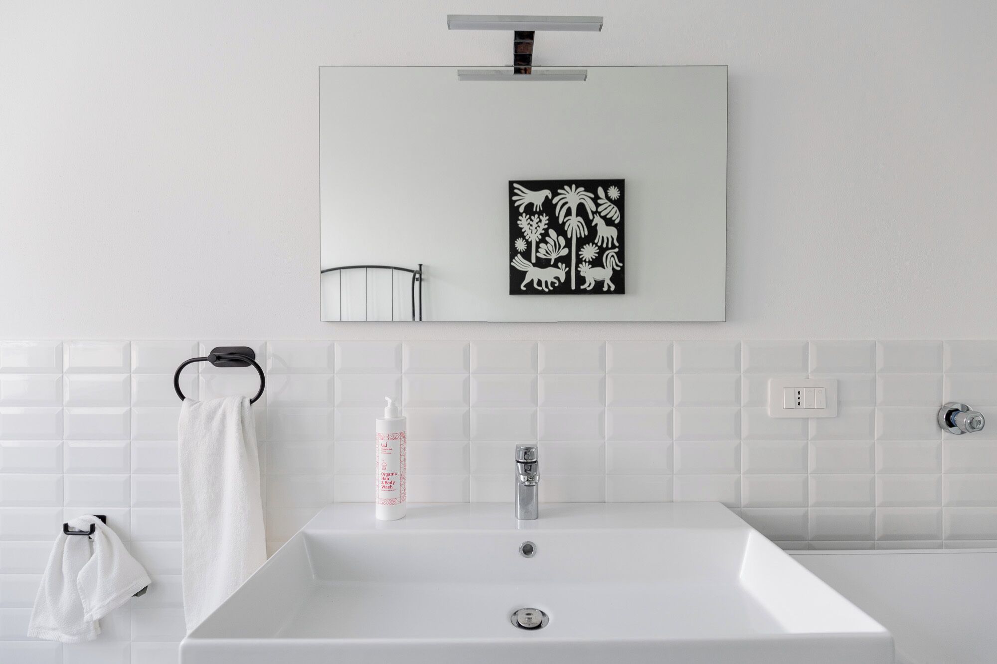 Une salle de bain avec un lavabo blanc, un miroir et une œuvre d’art murale représentant des animaux et des plantes.