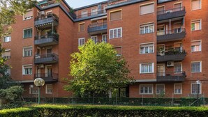 A multi-story brick apartment building with balconies, air conditioning units, and a green tree in the foreground. - A Casa di Giorgia II by Wonderful Italy (Bologna)