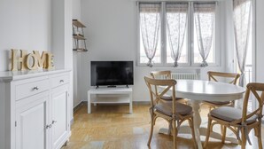 A dining area with a round table, four wooden chairs, a television on a stand, and a white cabinet with drawers. - A Casa di Giorgia II by Wonderful Italy (Bologna)